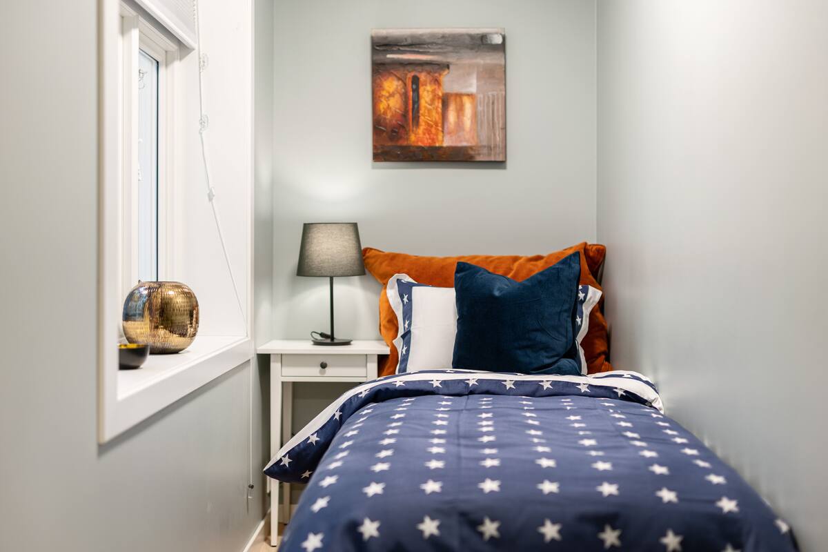Un dormitorio con cama, mesita de noche, lámpara y ventana.