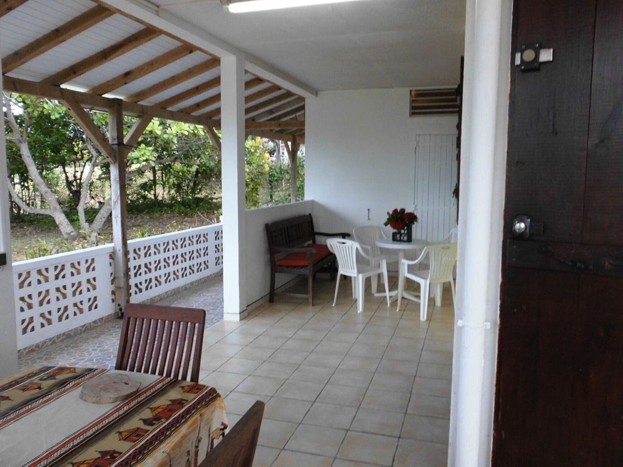 A covered patio area with a table and chairs, a bench, and a view of the outdoors.