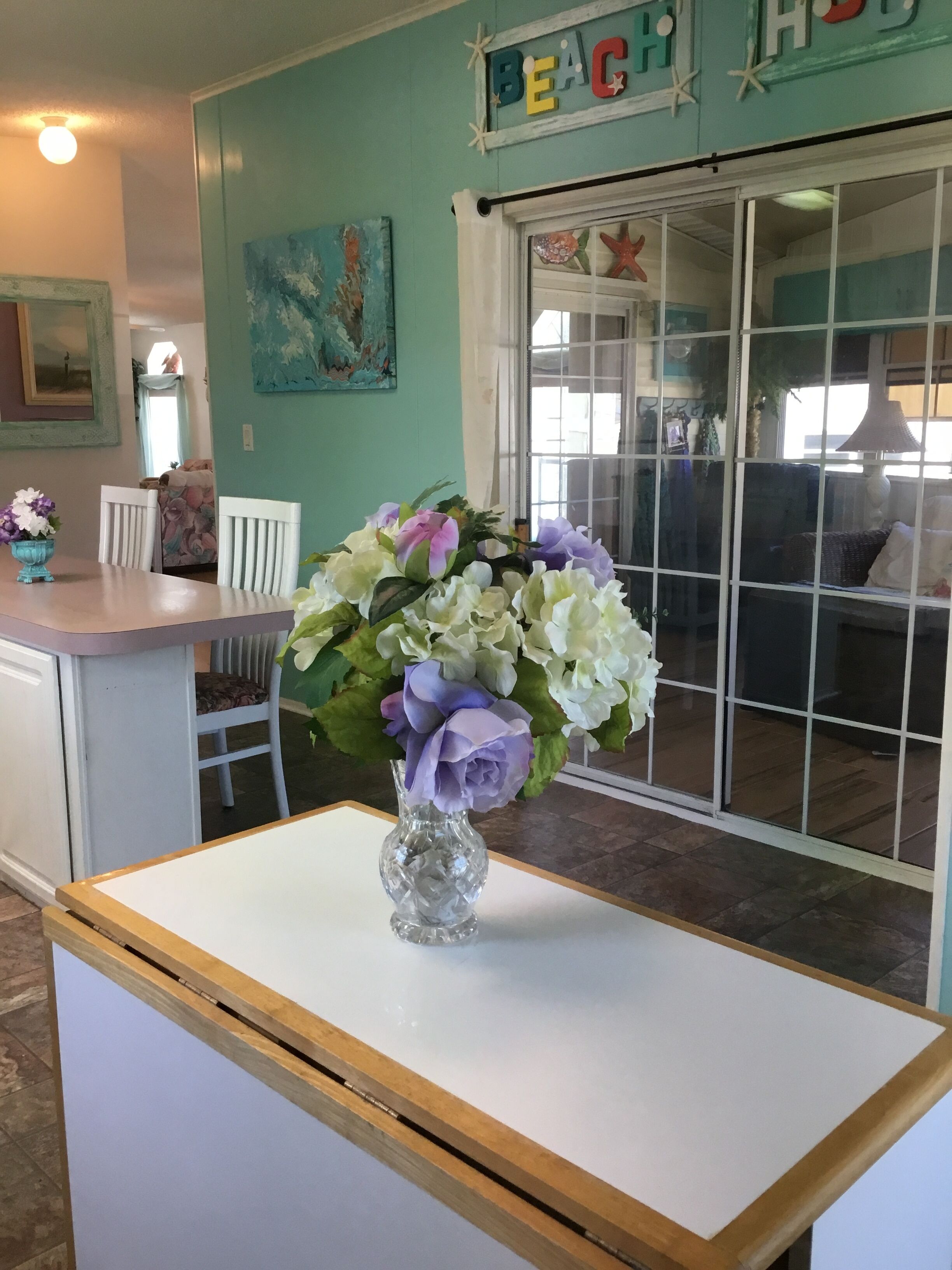 A room with teal walls, a white table with a vase of flowers, and a sign reading "BEACH HOUSE".
