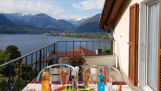 Un balcon avec une table préparée pour le petit-déjeuner, offrant une vue sur un lac et des montagnes.