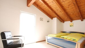 Une chambre avec un plafond en bois, un lit avec une literie jaune, une chaise noire et un petit tableau accroché au mur.