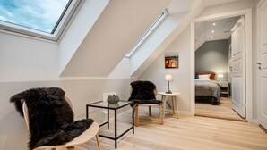 A modern loft bedroom with a skylight, a glass table, two chairs, and a bed.