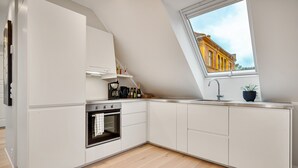A modern kitchen with white cabinetry, a built-in oven, a window with a view of a yellow building, and a black sink.
