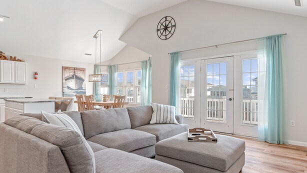 A spacious living room with a gray sectional sofa, a dining area with a table and chairs, and a kitchen in the background. - Gem of the Gold Coast. Book now and save for summer 2027!! Weeks will go fast!! (Ocean City)