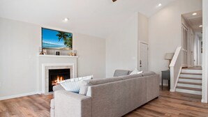 A living room with a fireplace, a sofa, and a staircase. - Gem of the Gold Coast. Book now and save for summer 2027!! Weeks will go fast!! (Ocean City)