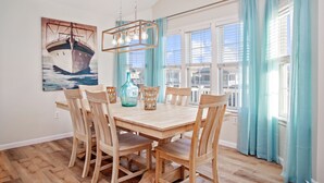 A dining area with a wooden table and chairs, a hanging light fixture, and a painting of a boat on the wall. - Gem of the Gold Coast. Book now and save for summer 2027!! Weeks will go fast!! (Ocean City)