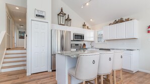 A modern kitchen with white cabinetry, stainless steel appliances, and a central island with bar stools. - Gem of the Gold Coast. Book now and save for summer 2027!! Weeks will go fast!! (Ocean City)