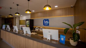 Un mostrador de recepción de hotel con computadoras, un mostrador de registro y un letrero del Hotel Tri.