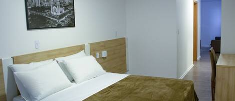 A hotel room with a bed, a desk, and a chair. There is a picture on the wall and an air conditioner above the bed.