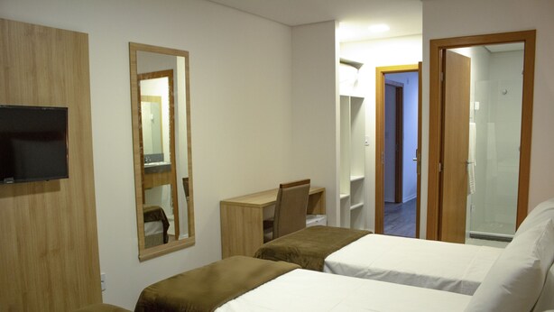 Habitación de hotel con dos camas, un escritorio, una silla, un televisor y un espejo.