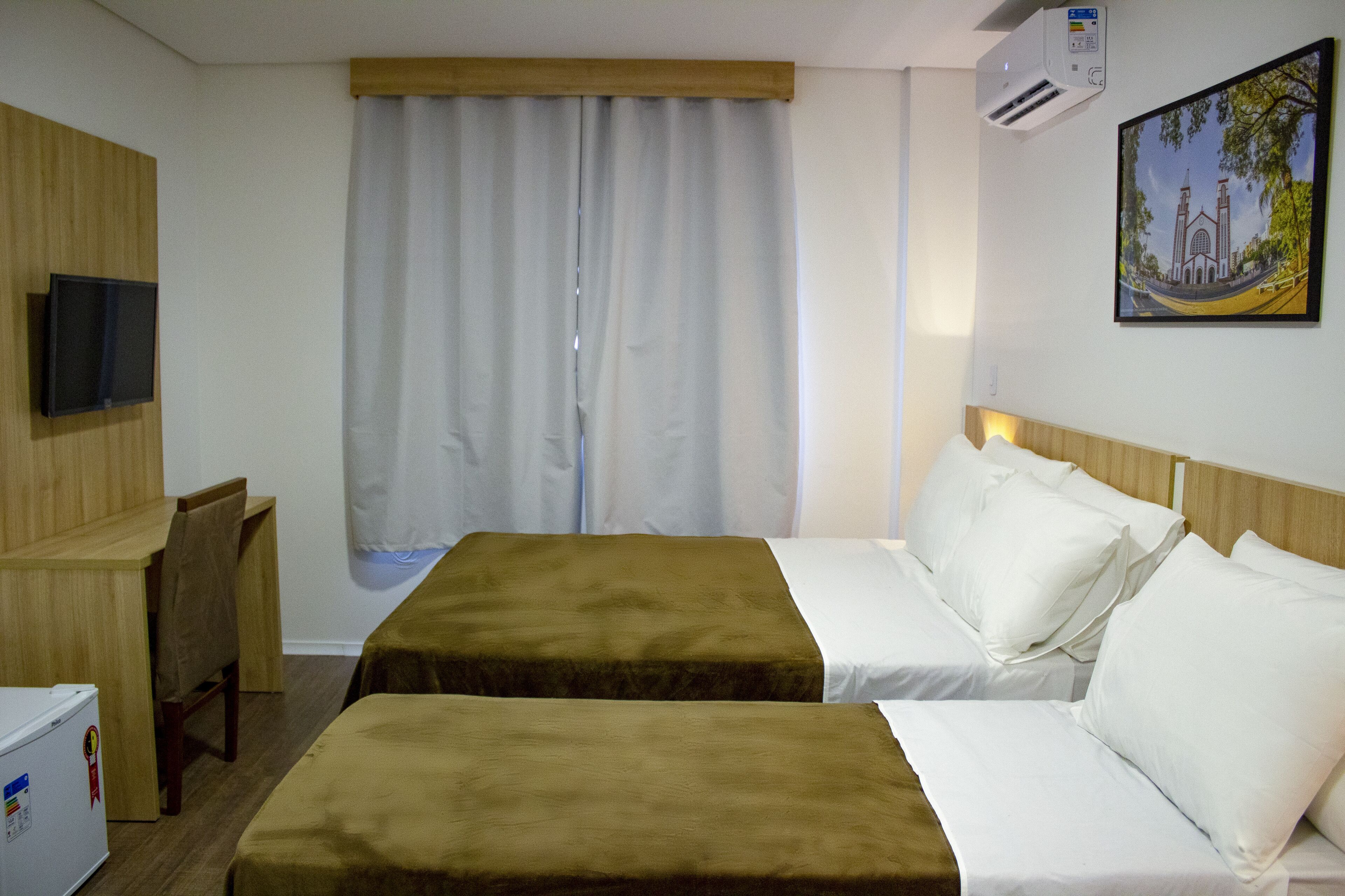 A hotel room with two beds, a desk, a chair, a television, and a painting on the wall.