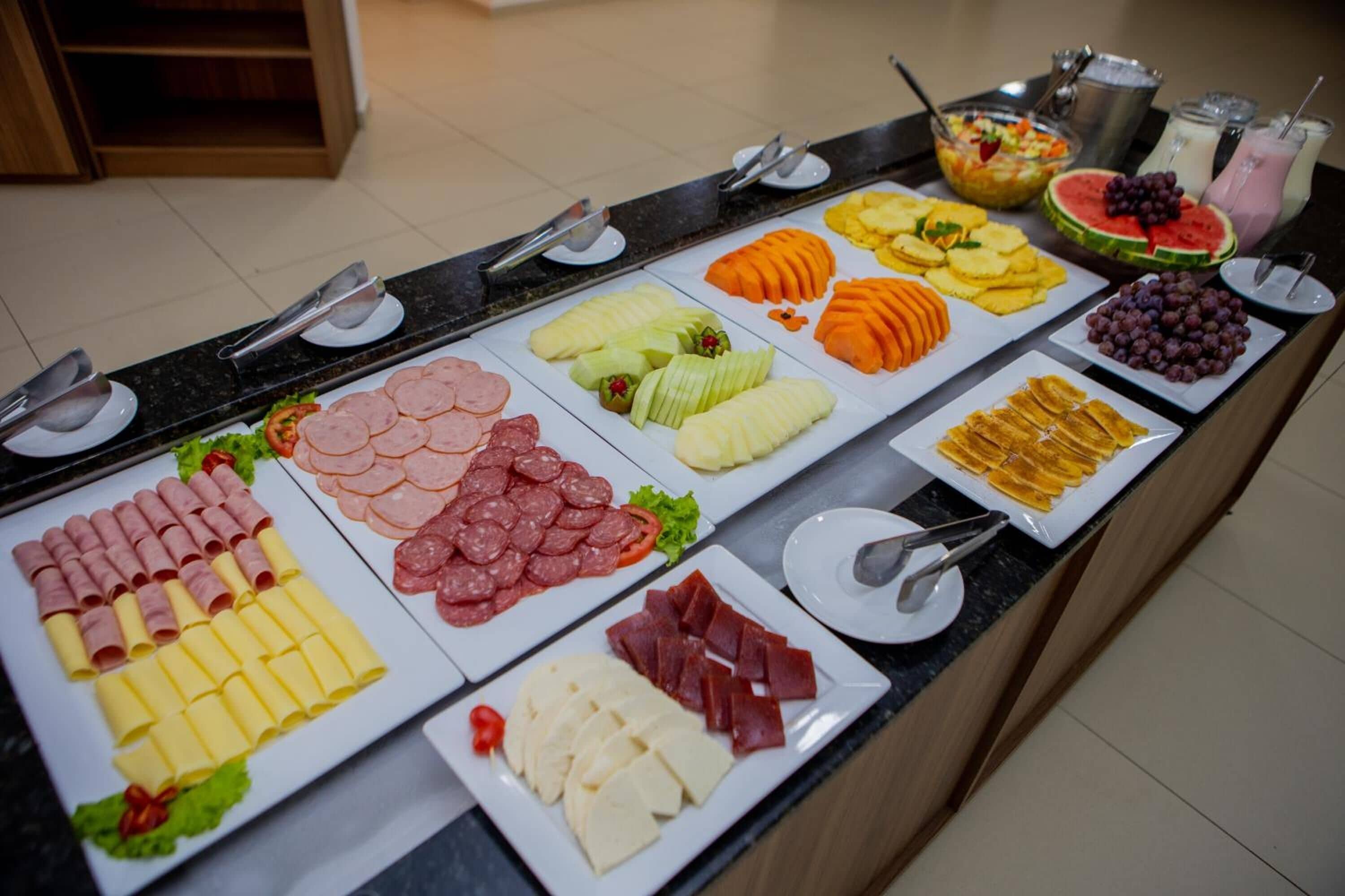Un bufé con diversas opciones de comida, incluyendo carnes, quesos, frutas y una ensalada.