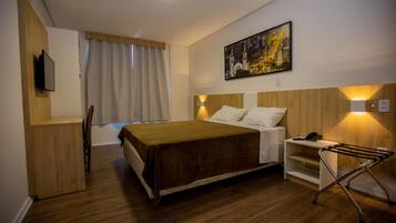 A hotel room with a bed, a desk, a chair, a TV, and a painting on the wall.
