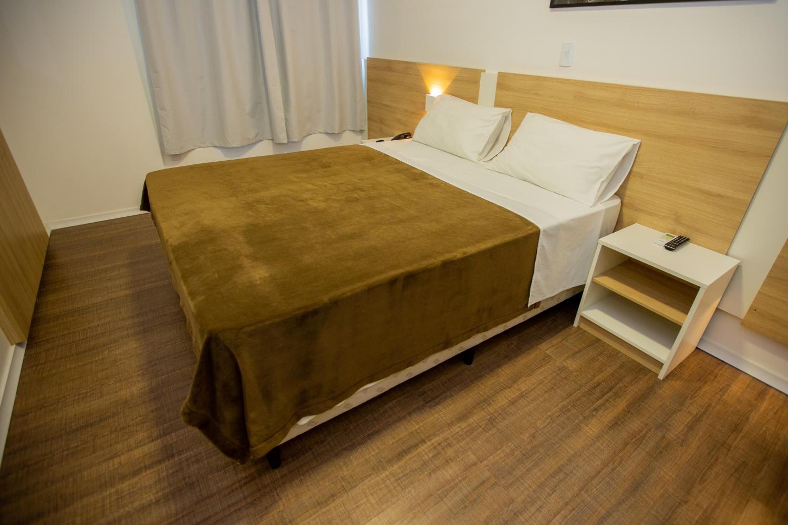 Una habitación de hotel con una cama, una mesita de noche y suelo de madera.