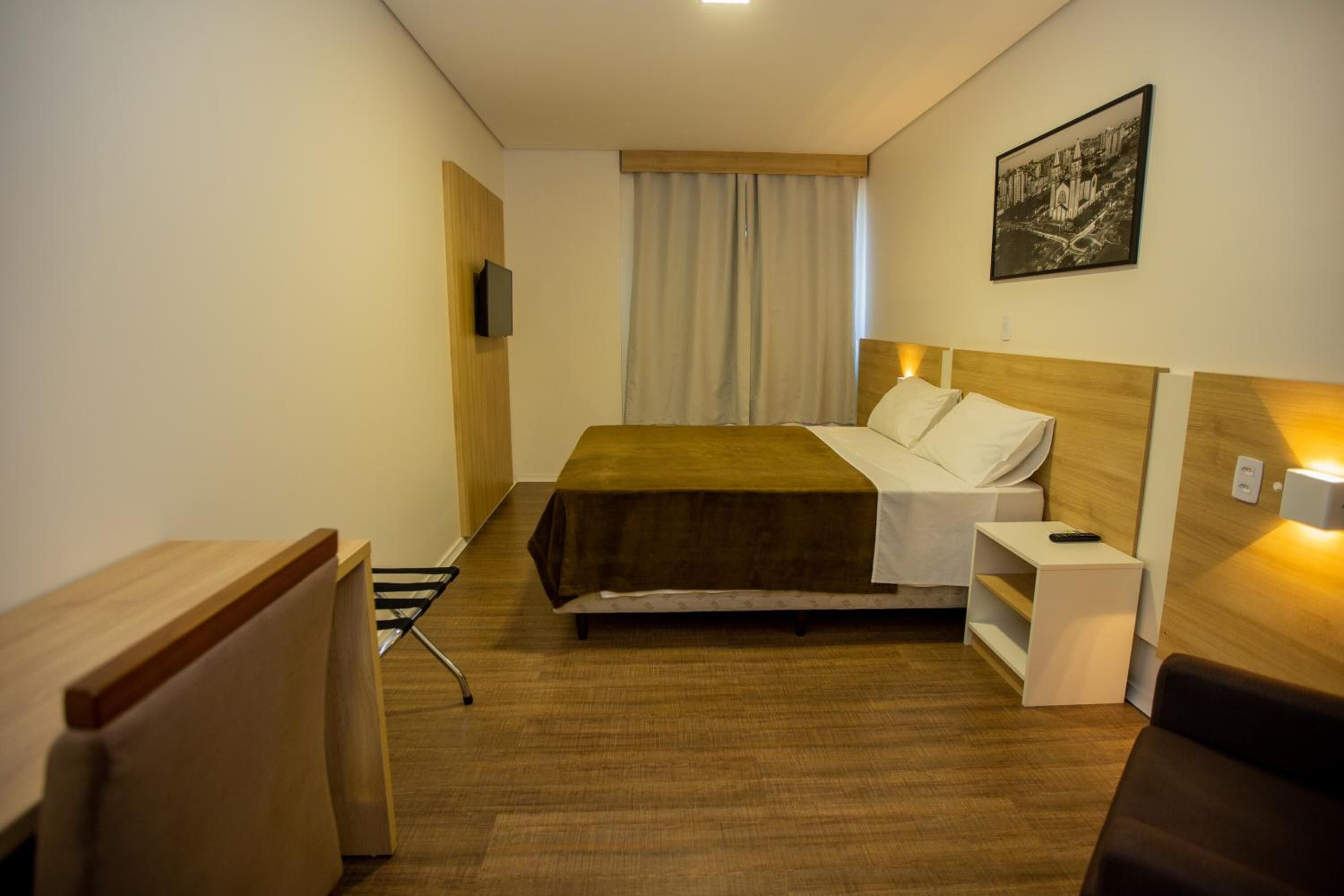 A hotel room with a bed, bedside table, and a television on the wall.