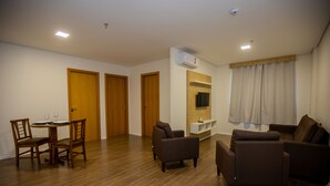 Una sala de estar con una mesa de comedor, dos sillones, un sofá, piso de madera, un televisor montado en la pared y un aire acondicionado instalado en el techo.