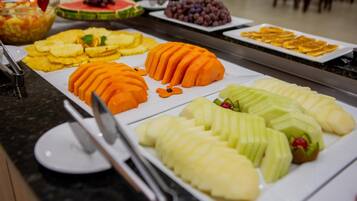 A buffet with various fruits and vegetables, including sliced apples, oranges, and bananas.