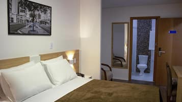 Habitación de hotel con cama, mesita de noche, teléfono, espejo y baño visible a través de una puerta abierta.