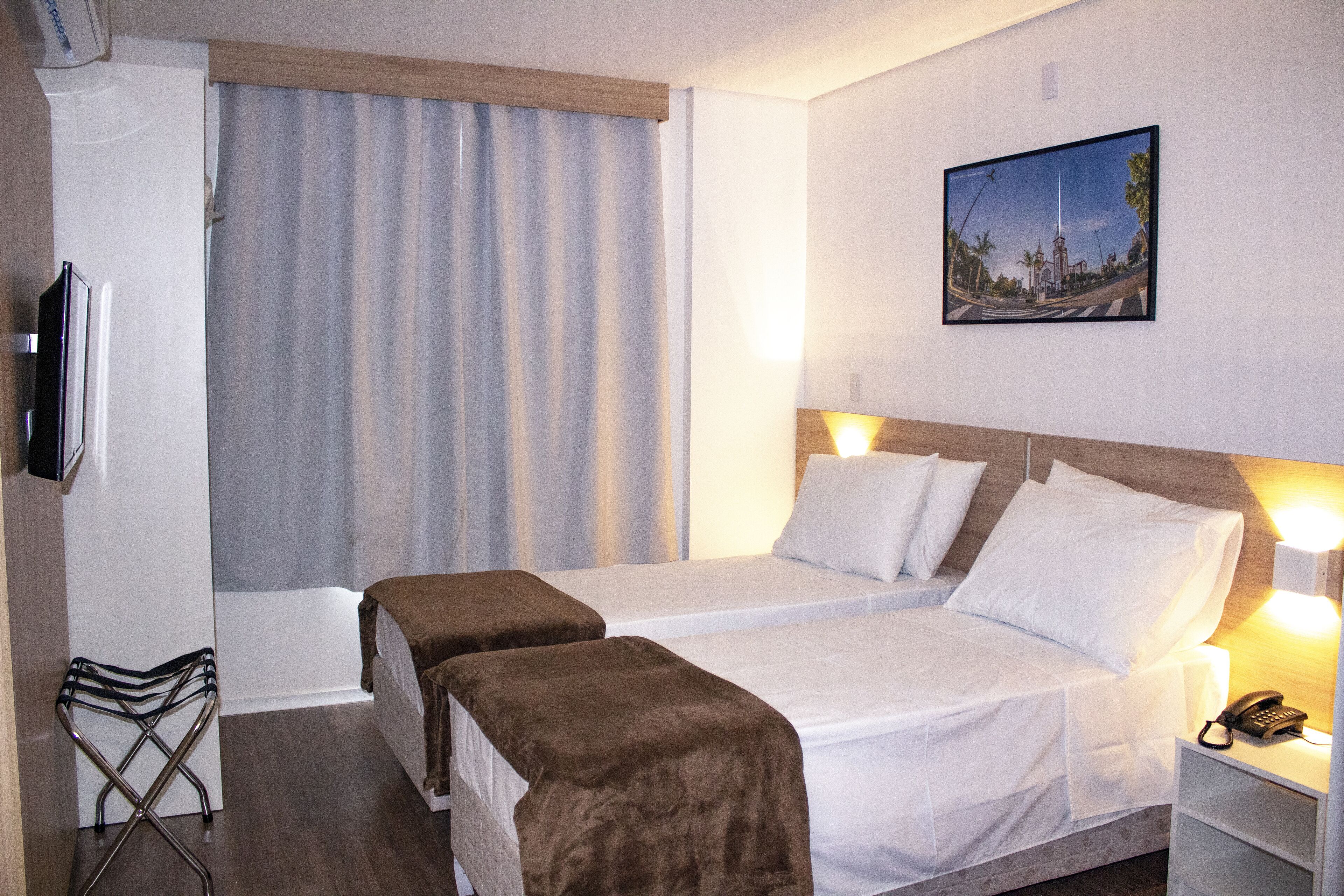 Une chambre d’hôtel avec deux lits, une télévision, un bureau avec une lampe et un tableau au mur.