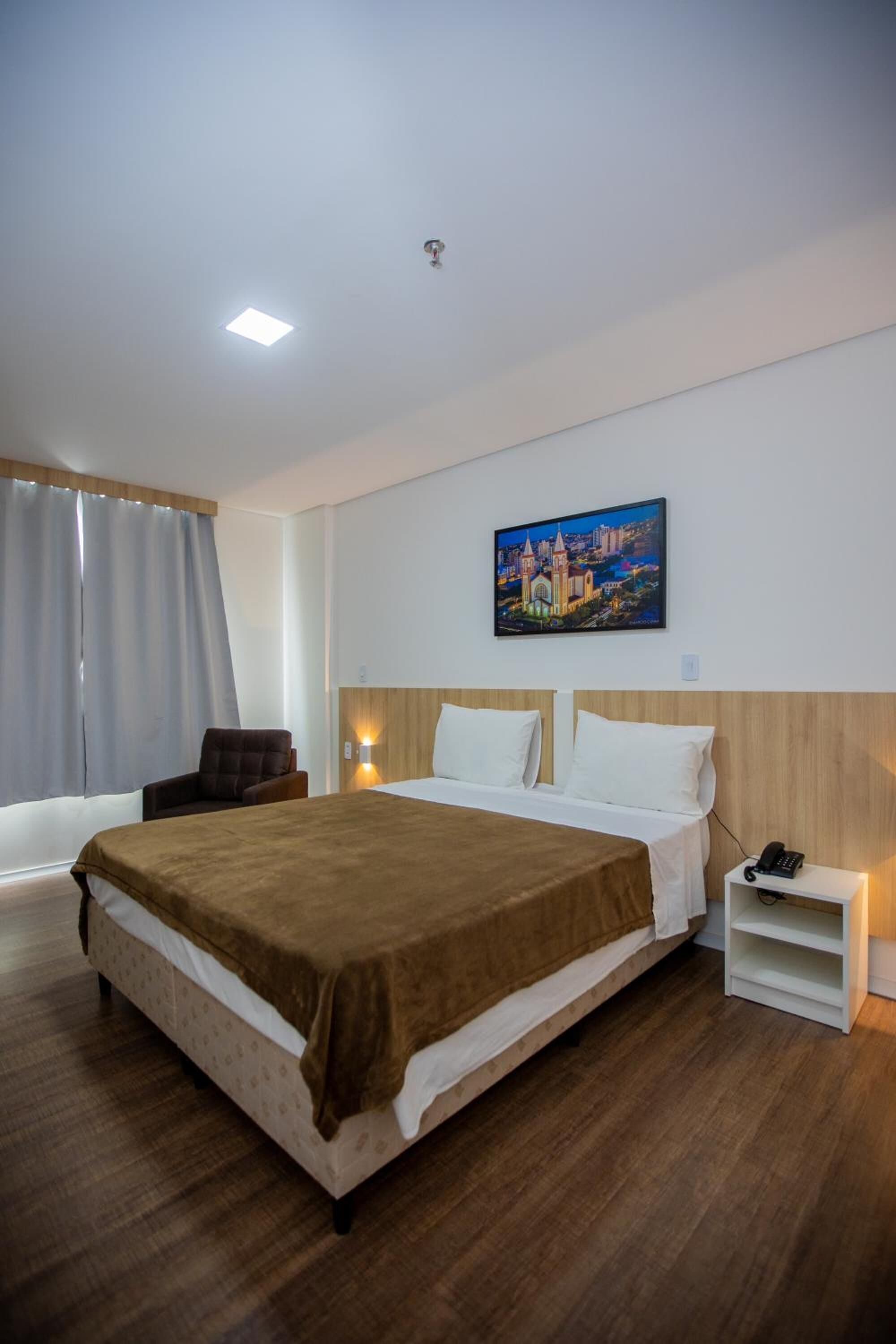 A hotel room with a large bed, a chair, a nightstand, and a painting on the wall.