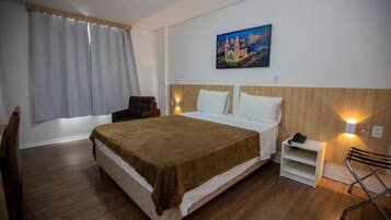 Una habitación de hotel con una cama grande, una silla, una mesita de noche con un teléfono y un cuadro en la pared.