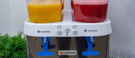 A dual-blender with two transparent containers, one with orange liquid and the other with red liquid, on a kitchen counter.