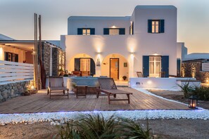 A modern house with a wooden deck, outdoor seating, and stone walls.