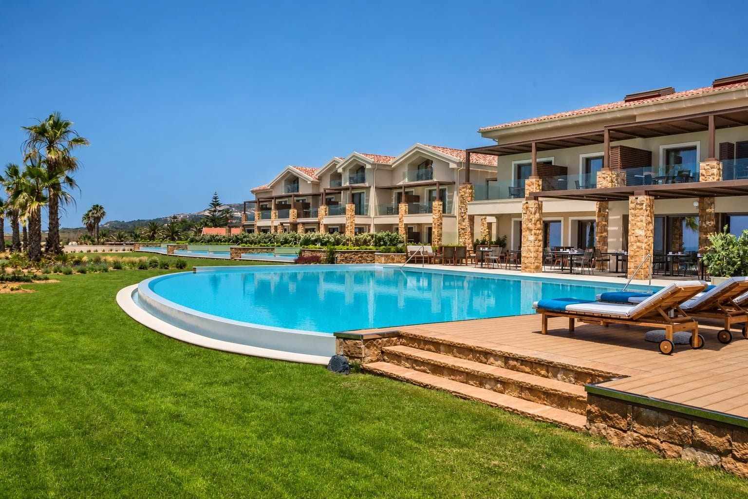 Una piscina de borde curvo, rodeada por un césped cuidado y un patio con sillones de descanso.