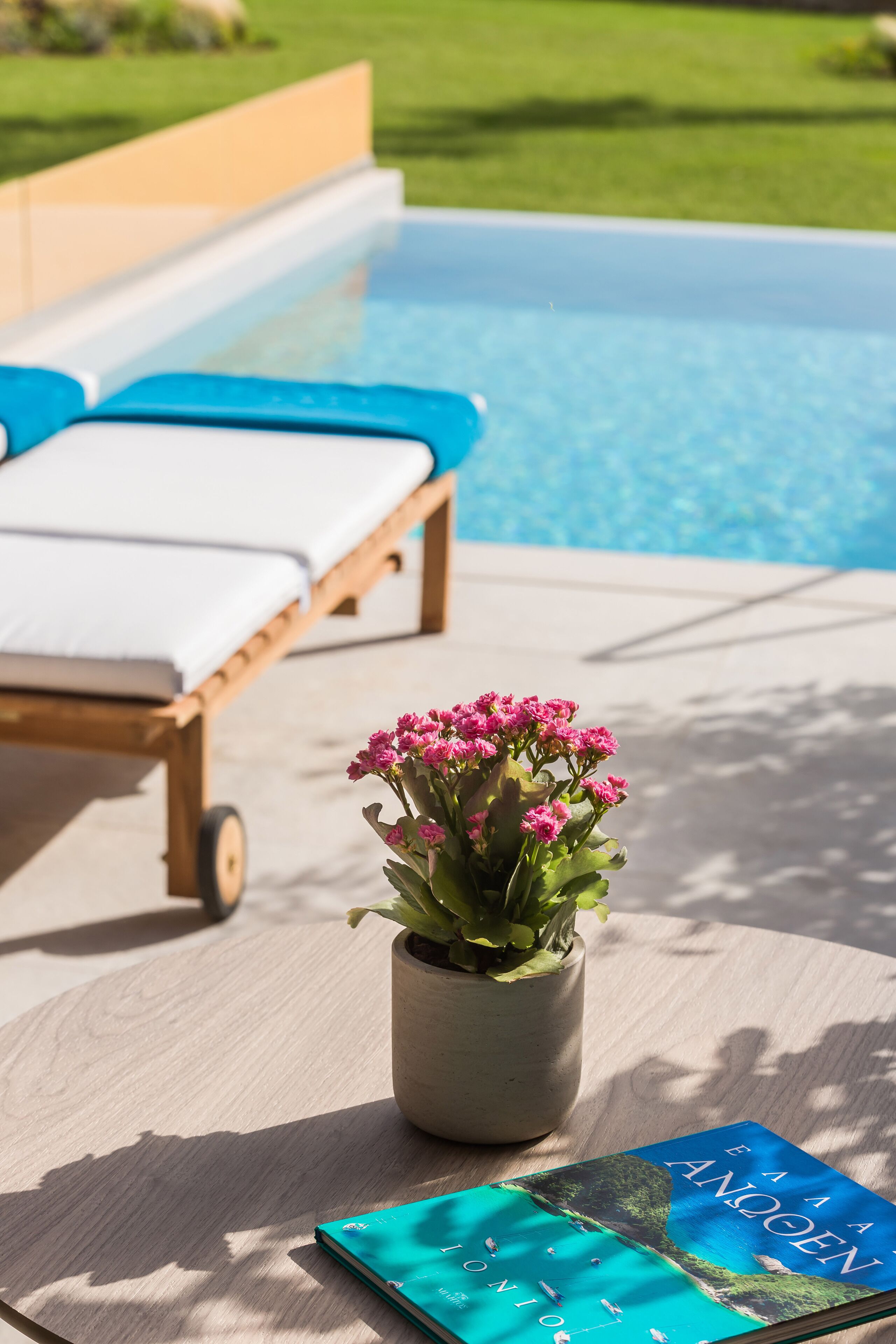 A poolside area with a lounge chair, a small table with a book, and a potted plant.