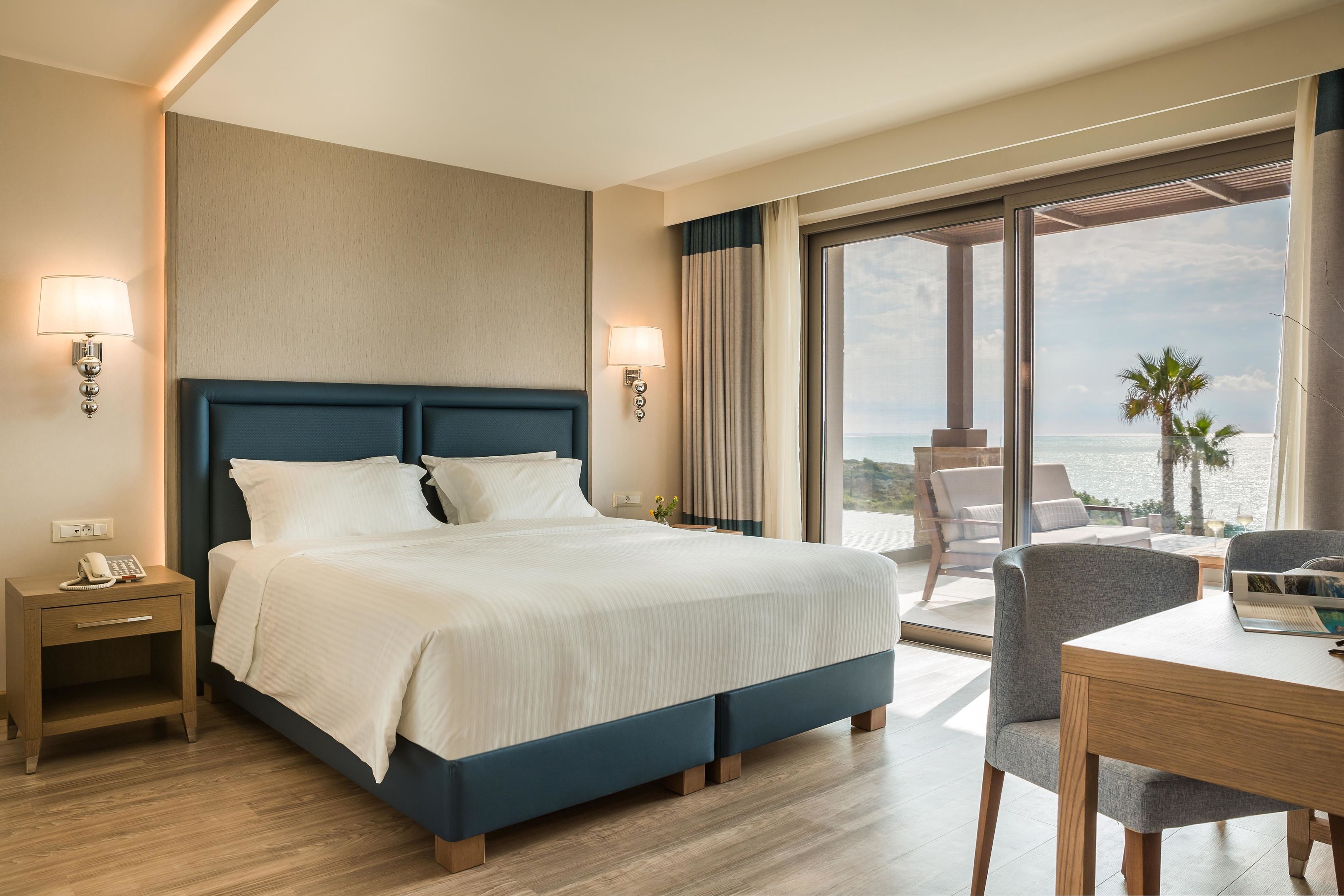 Una habitación de hotel con una cama grande, lámparas de noche, un escritorio y vista al océano.