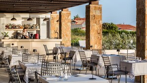 Un espace extérieur aménagé pour les repas, avec des tables et des chaises, un bar proposant une variété de boissons, et une vue sur le paysage environnant.