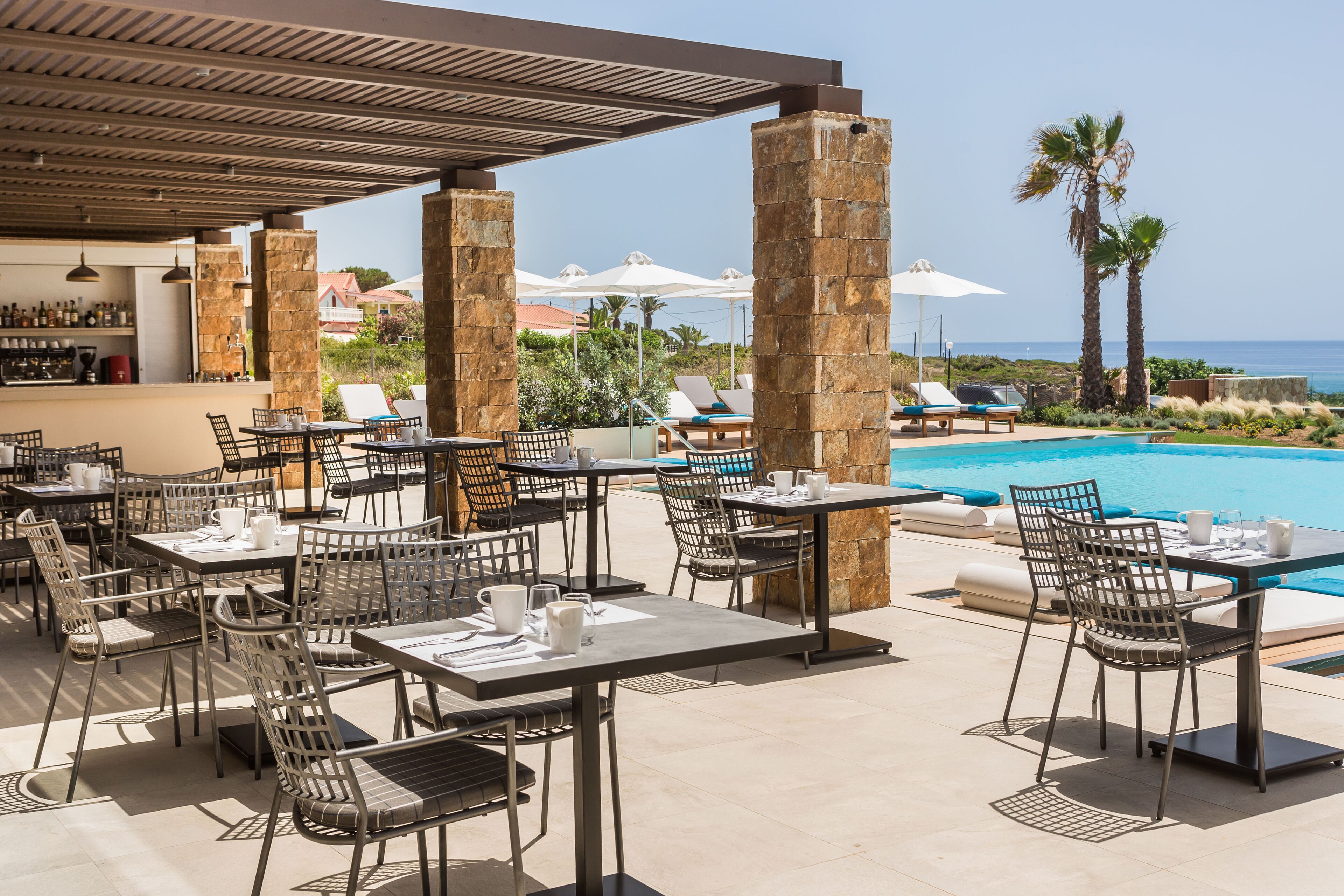 An outdoor dining area with tables and chairs, a pool, and umbrellas.