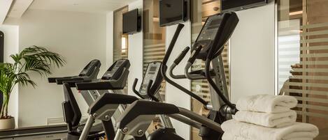 Un gimnasio con cintas de correr, una bicicleta estática y un televisor montado en la pared.