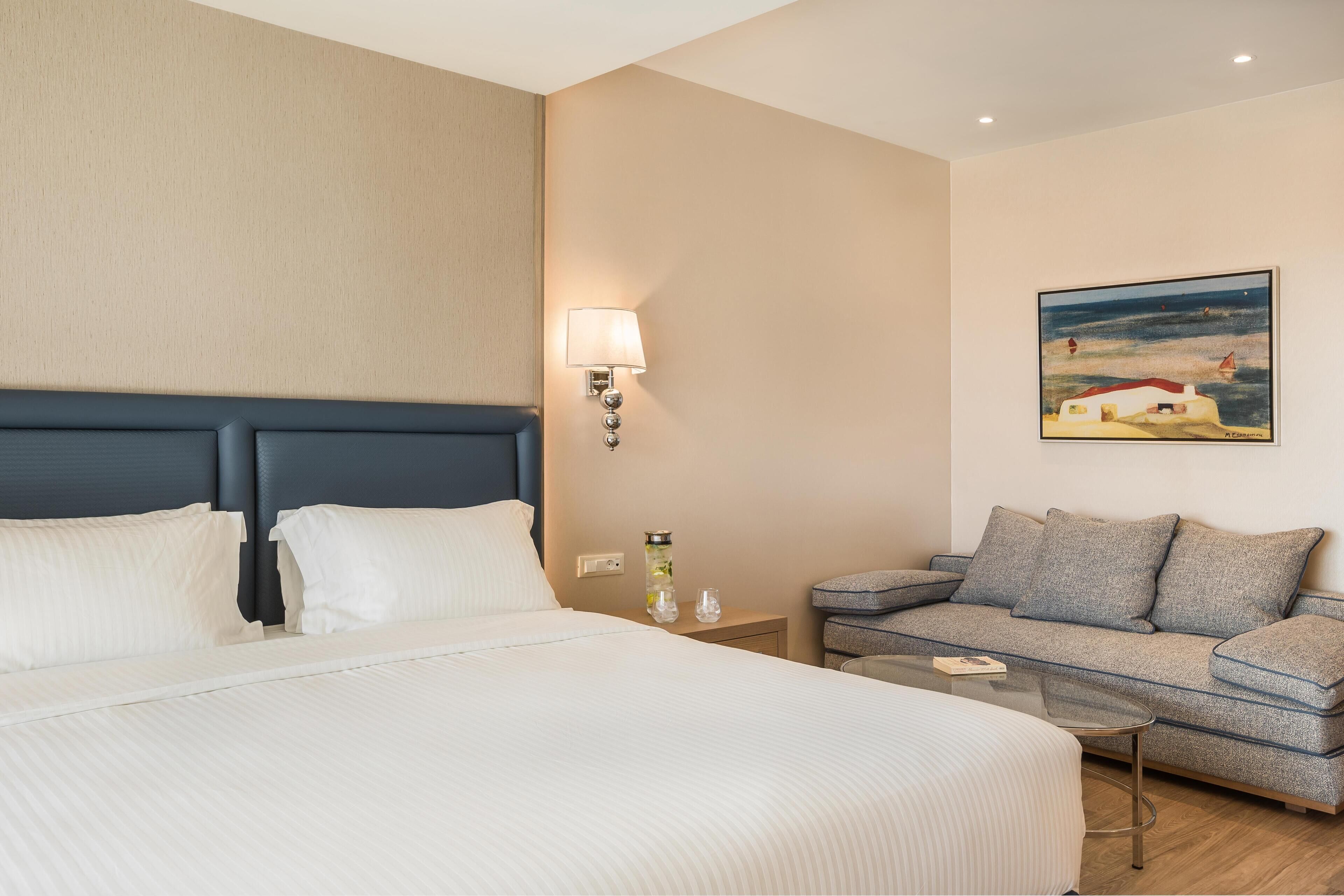 Ein Hotelzimmer mit Bett, Sofa, Nachttisch, Lampe und einem Bild an der Wand.