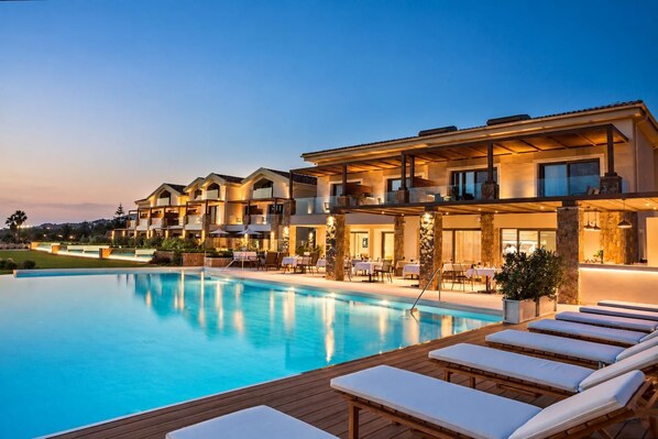 A hotel with a swimming pool, outdoor seating, and a well-lit facade.