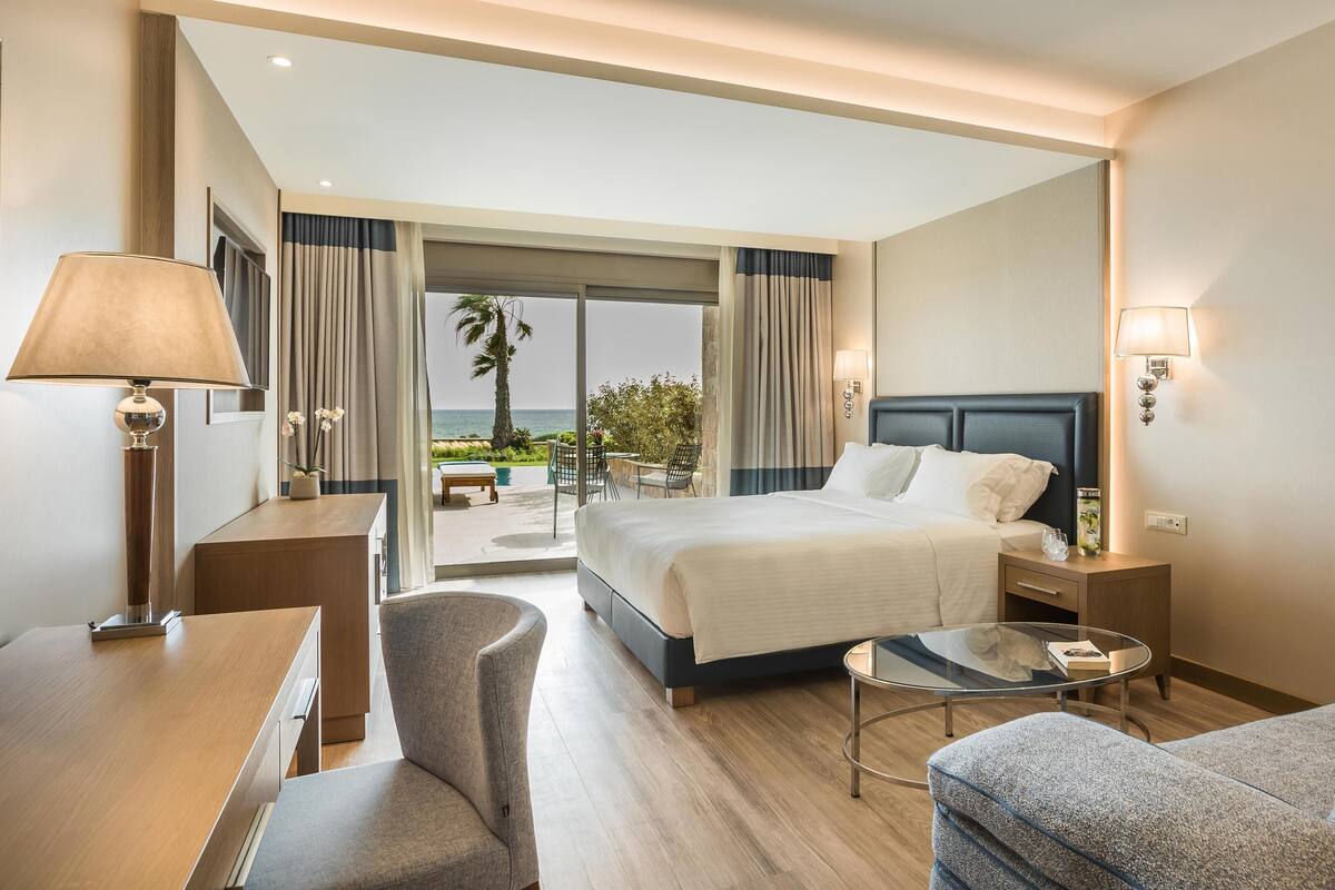 Een hotelkamer met een bed, een bureau, een stoel, een klein tafeltje en uitzicht op het omliggende landschap.