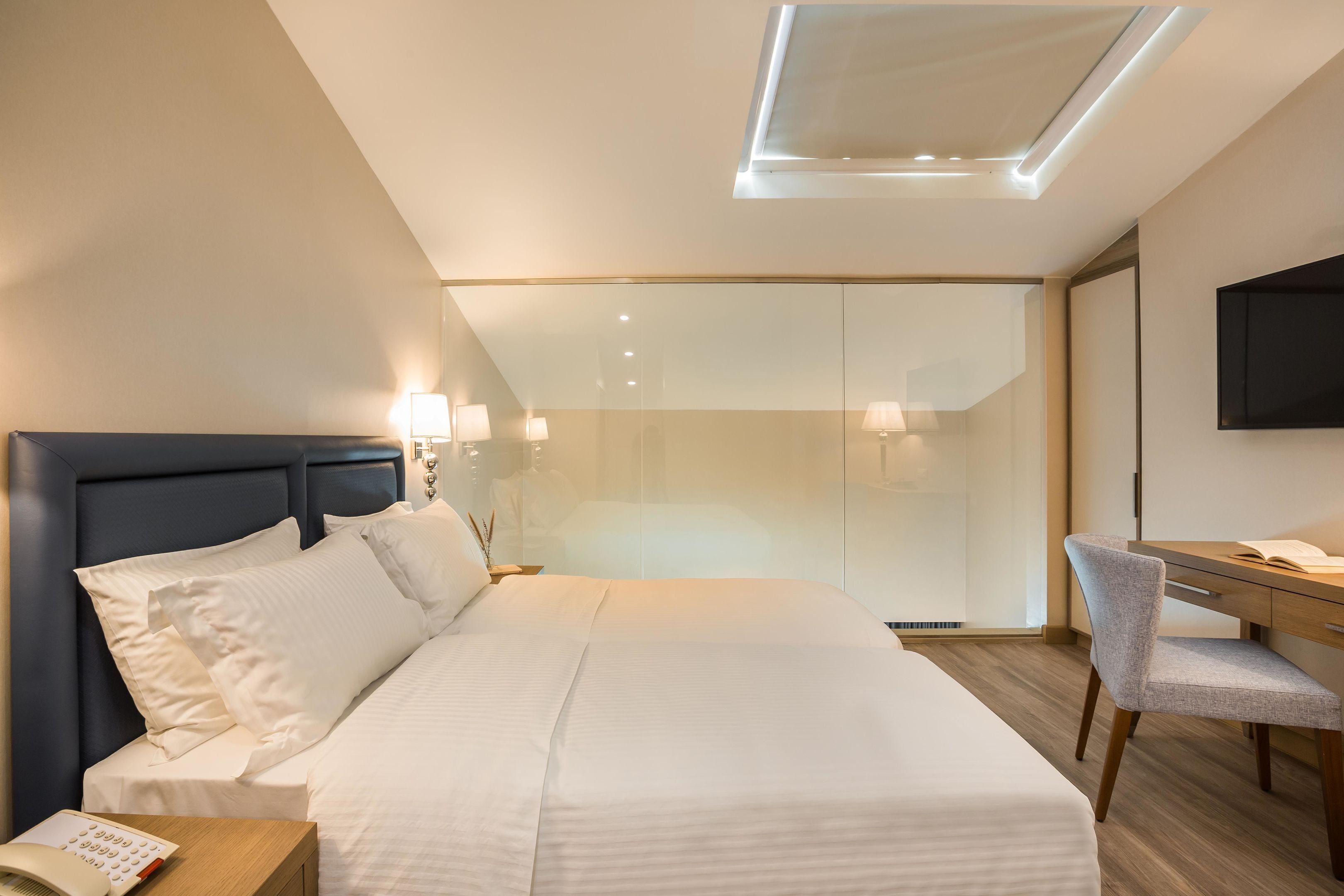 Een moderne hotelkamer met een groot bed, nachtkastje, lamp en bureau met stoel.