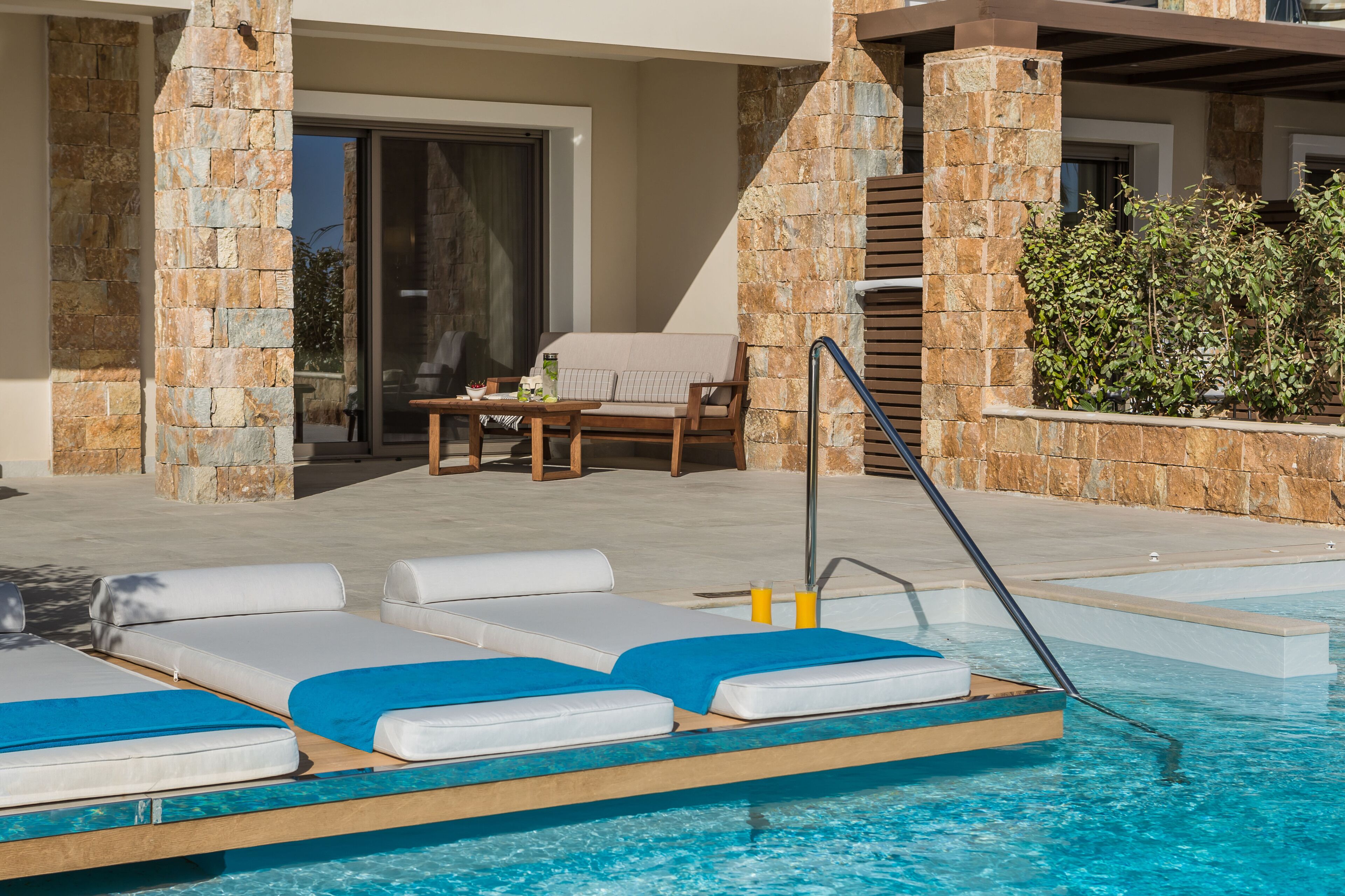 A poolside area with lounge chairs, a table, and a staircase leading to a covered deck.