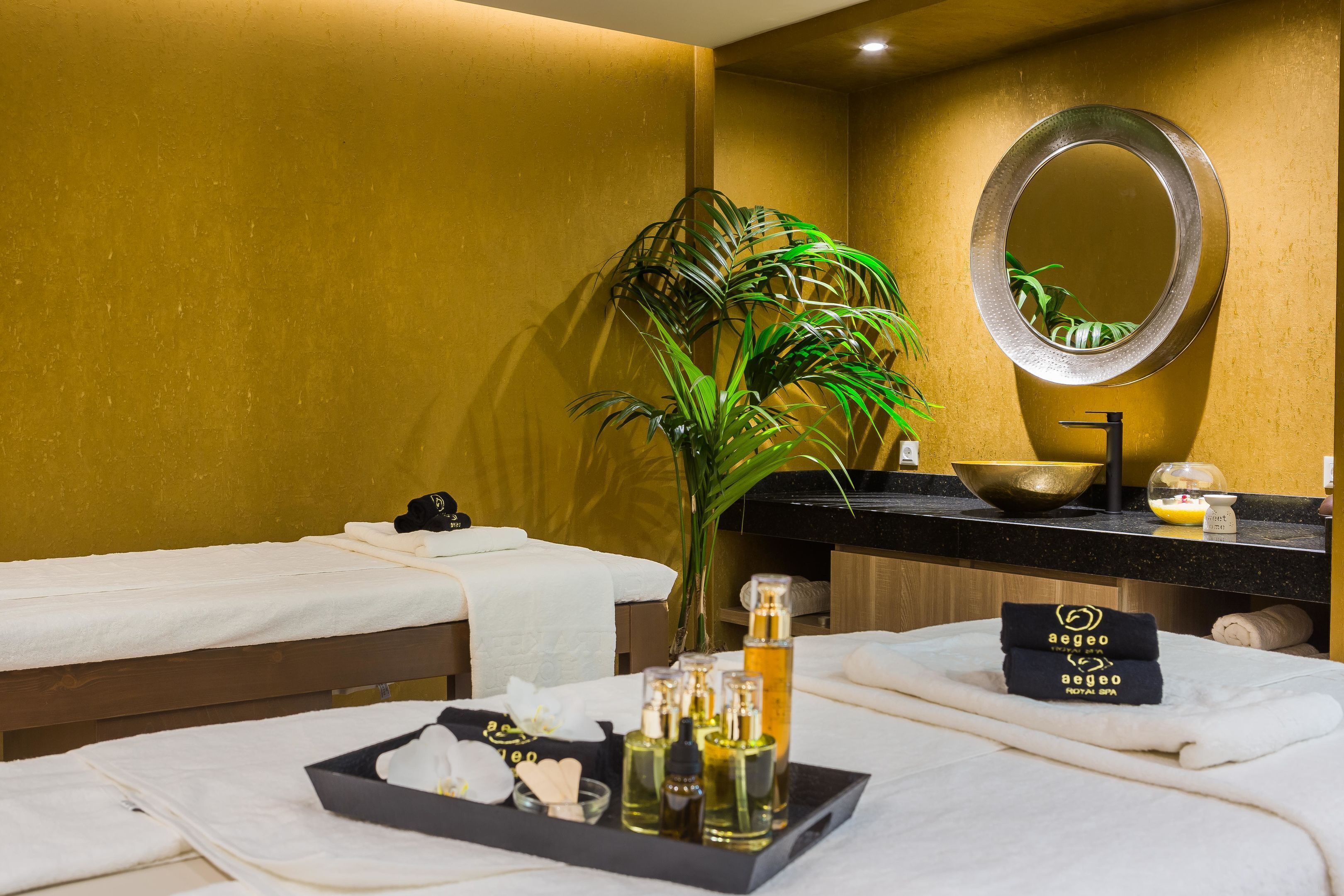 A hotel room with a massage table, a large mirror, a plant, and a tray with toiletries.