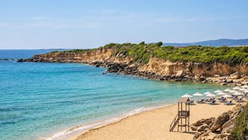 Une plage à l’eau turquoise et limpide, avec un rivage sablonneux, et un poste de surveillance des sauveteurs équipé de parasols et de chaises longues.