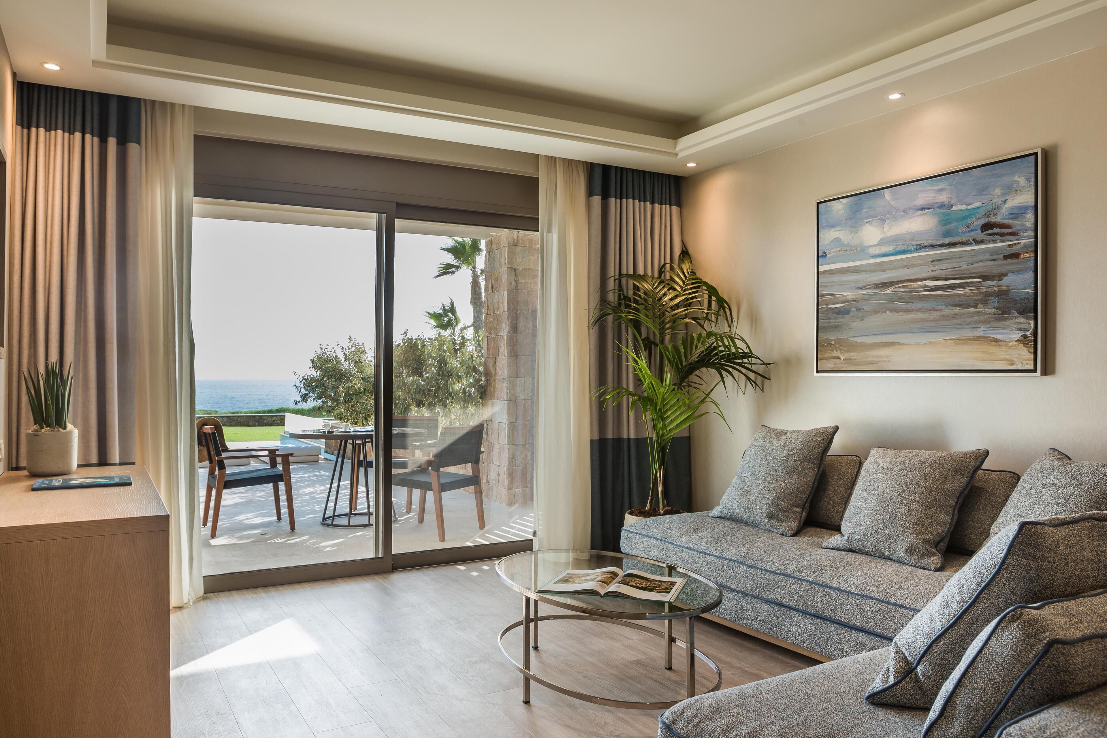 Una sala de estar moderna con un sofá, una mesa de centro y vistas al exterior a través de un gran ventanal corredizo.