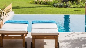 Un espace aménagé au bord de la piscine, avec deux chaises longues, un palmier et une vue sur l’océan.