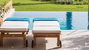 Un espace aménagé au bord de la piscine, avec deux chaises longues, un palmier et une vue sur l’océan.