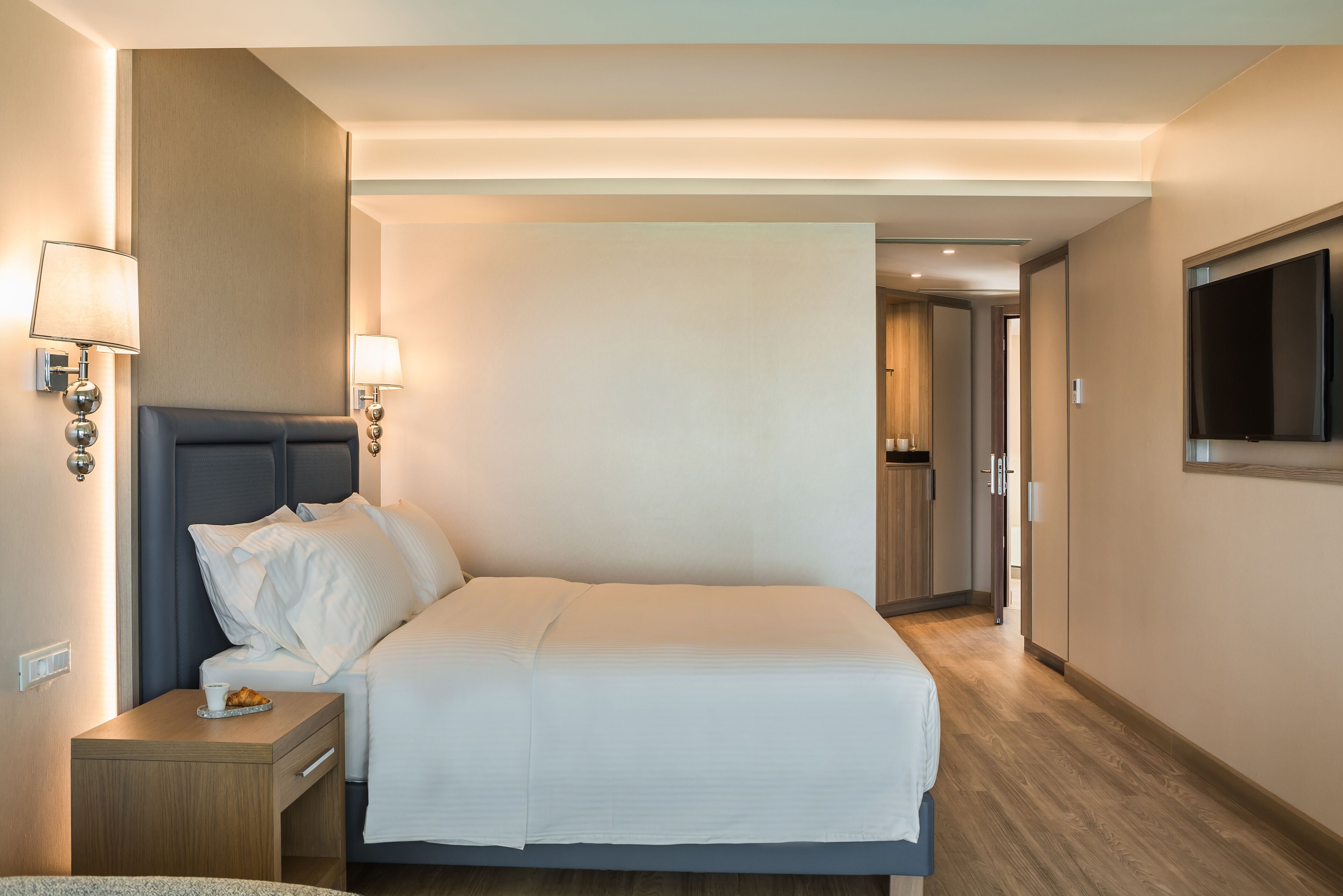 A hotel room with a bed, bedside tables, a TV, and a hallway leading to a bathroom.