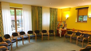 Un salón de conferencias con filas de sillas, una mesa con un atril y un ventanal con cortinas.