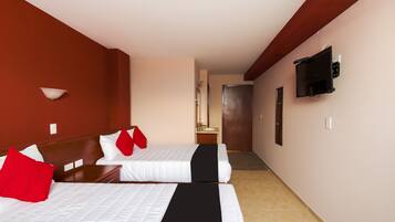 Une chambre d’hôtel avec deux lits, une télévision, un miroir et une salle de bain visible au fond.