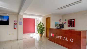 A reception area with a wooden reception desk labeled "CAPITAL O," a potted plant, a fire extinguisher, and a television on the wall.