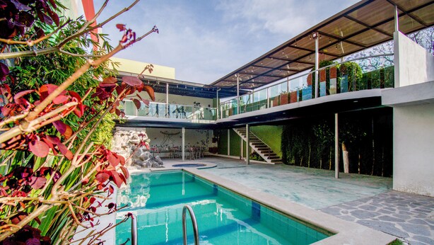 A modern pool area with a clear pool, stone steps, and a covered seating area. - Hotel San Pablo (San Pedro Cholula)