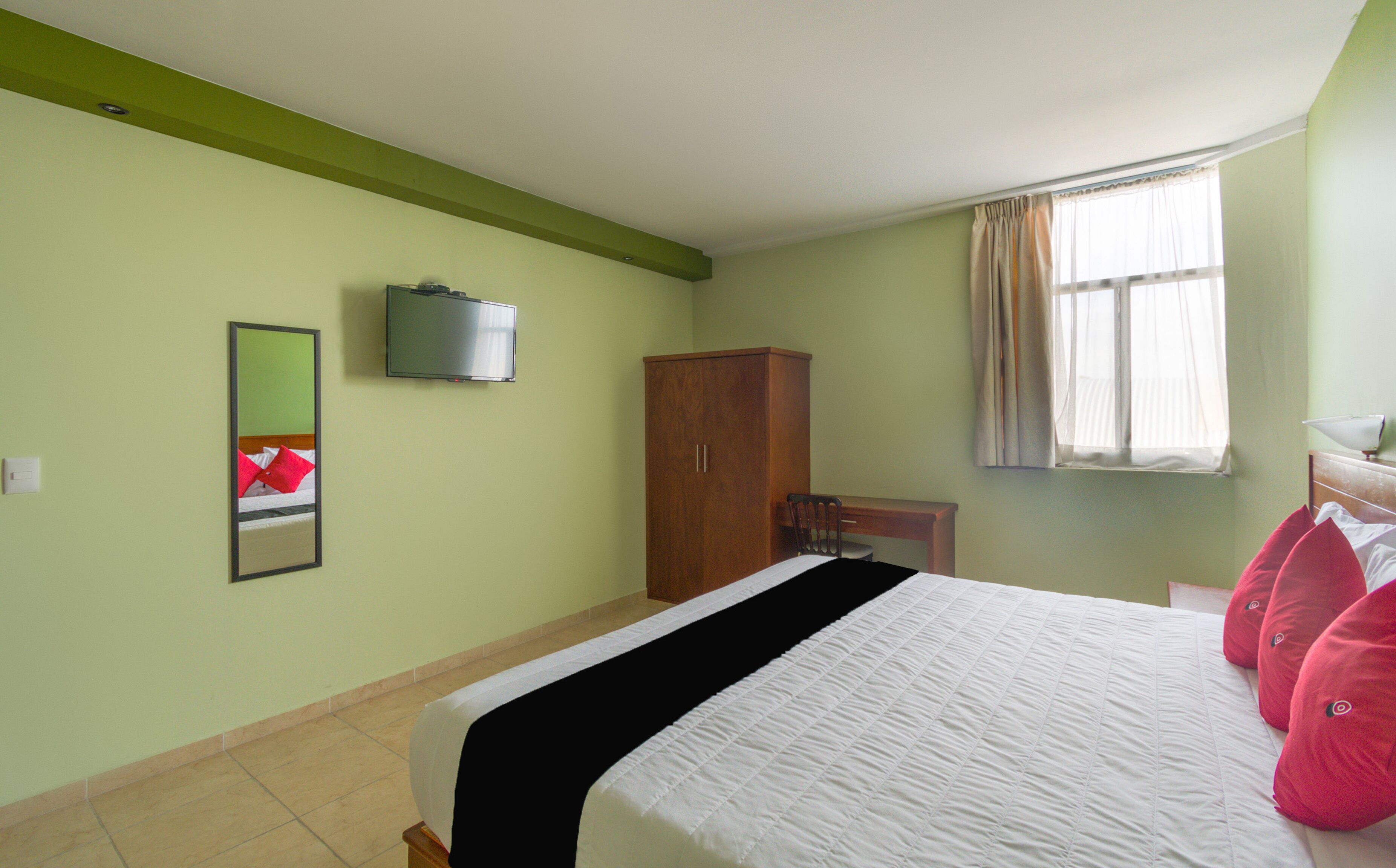 Habitación de hotel con cama, televisión en la pared, armario de madera, una silla y una ventana con cortinas.
