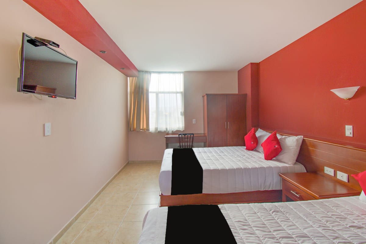 A hotel room with two beds, a desk, a chair, a wardrobe, and a TV mounted on the wall.